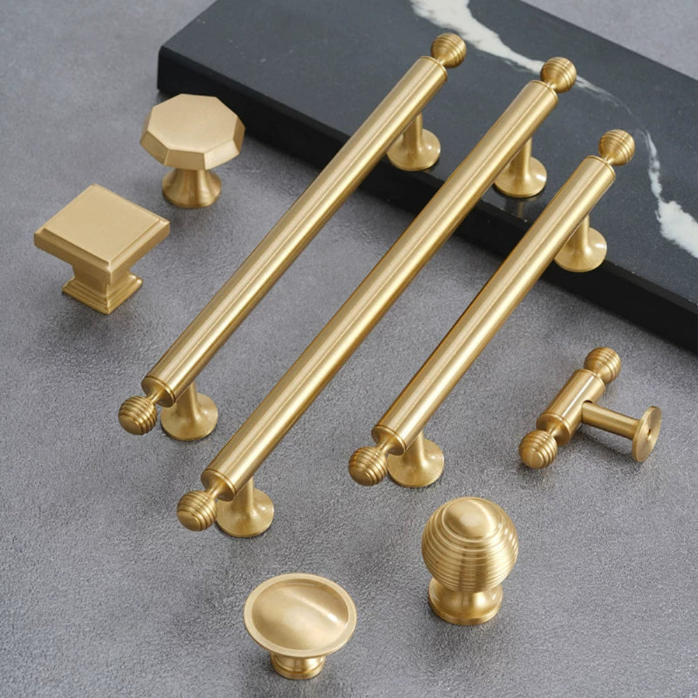 Collection of gold cabinet handles and knobs on a gray surface