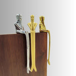 Three metallic figures in different colors (silver, gold, and bronze) on a wooden surface with a gray background.