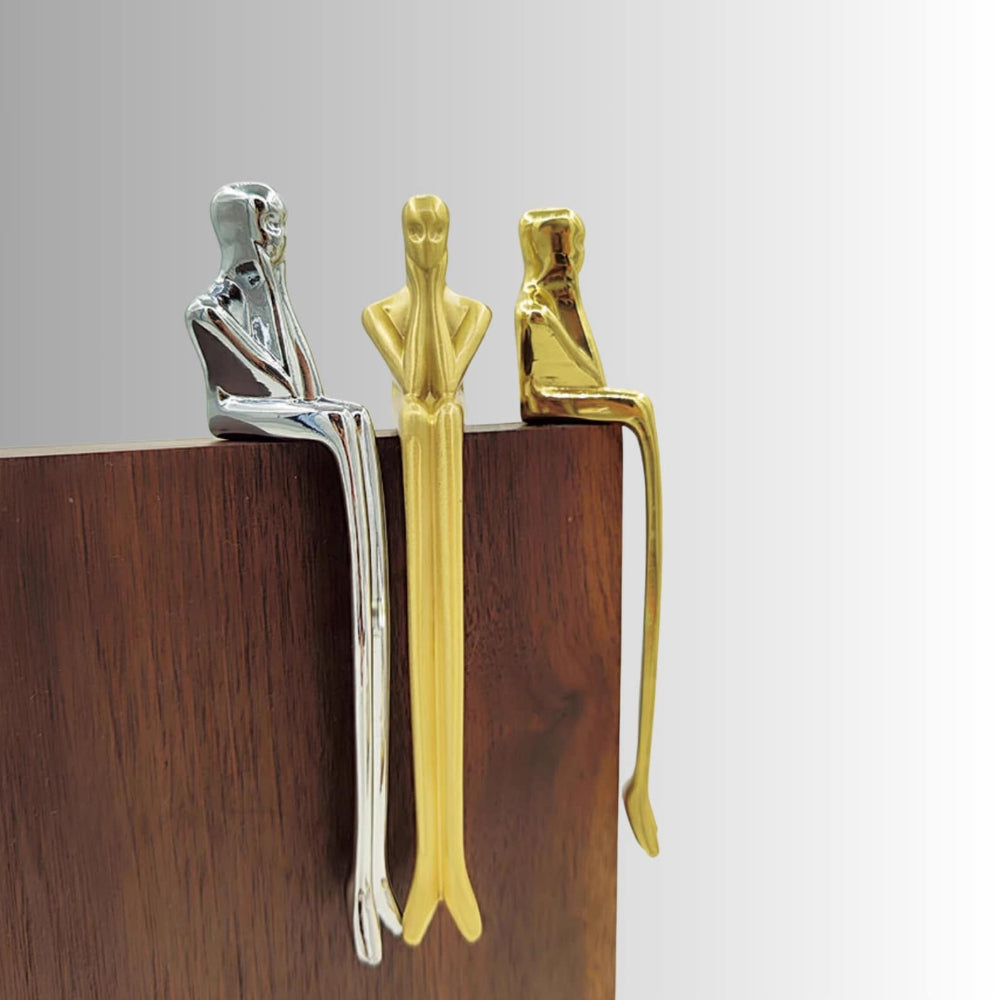 Three metallic figures in different colors (silver, gold, and bronze) on a wooden surface with a gray background.