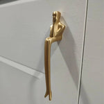 Gold door handle shaped like a stylized human figure on a white door.