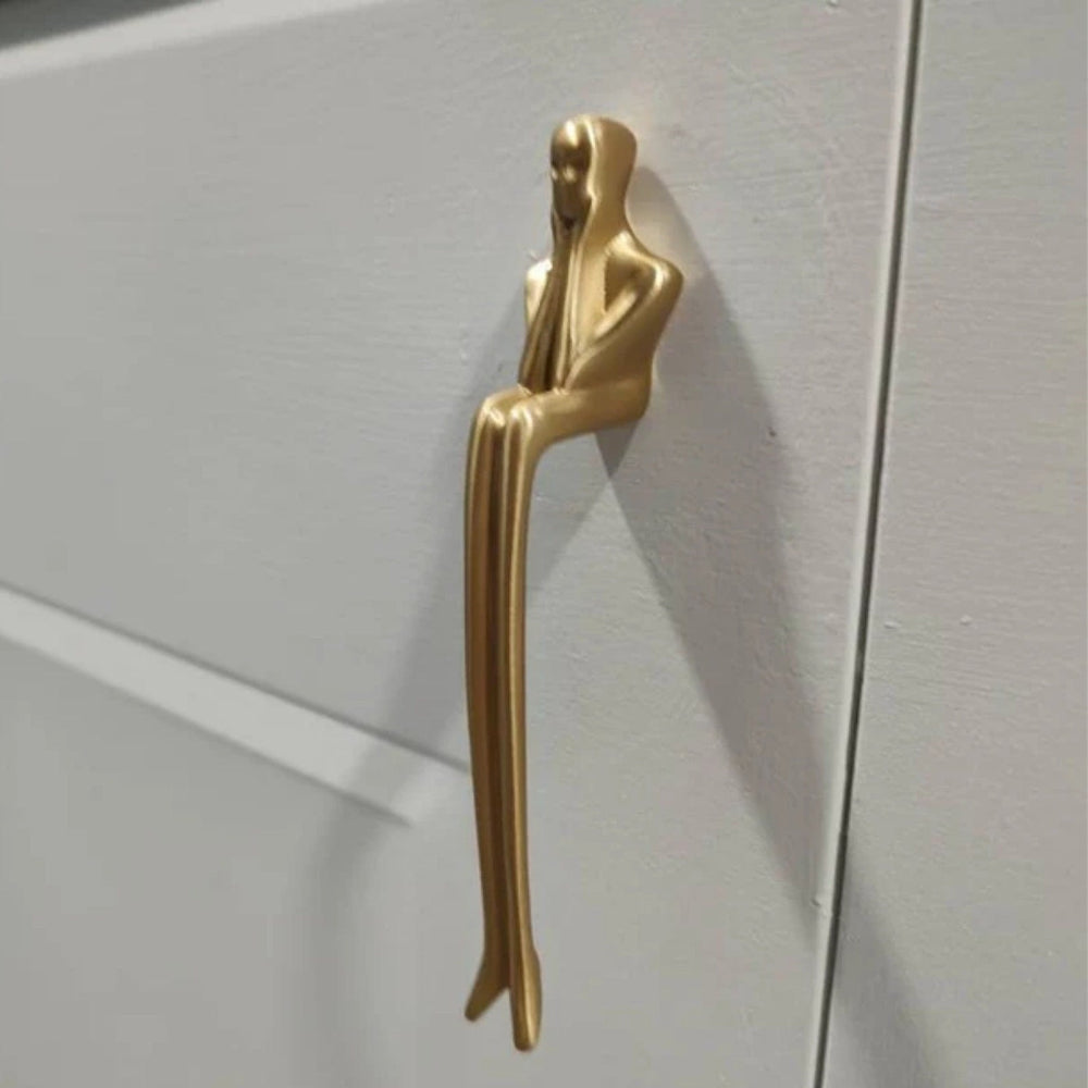 Gold door handle shaped like a stylized human figure on a white door.