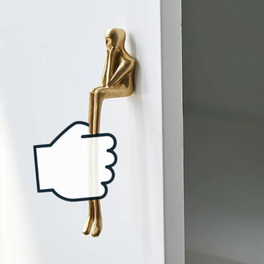 Gold door handle shaped like a sitting person on a white door