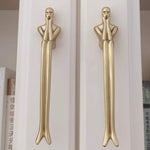 Two gold door handles shaped like human figures on a white background