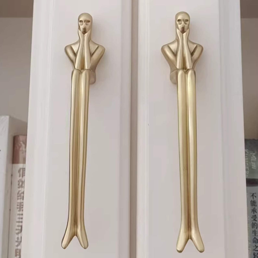 Two gold door handles shaped like human figures on a white background
