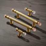 Gold cabinet handles with pink glass knobs on a wooden surface