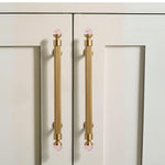 Cabinet doors with gold handles featuring pink glass knobs on a light beige background.