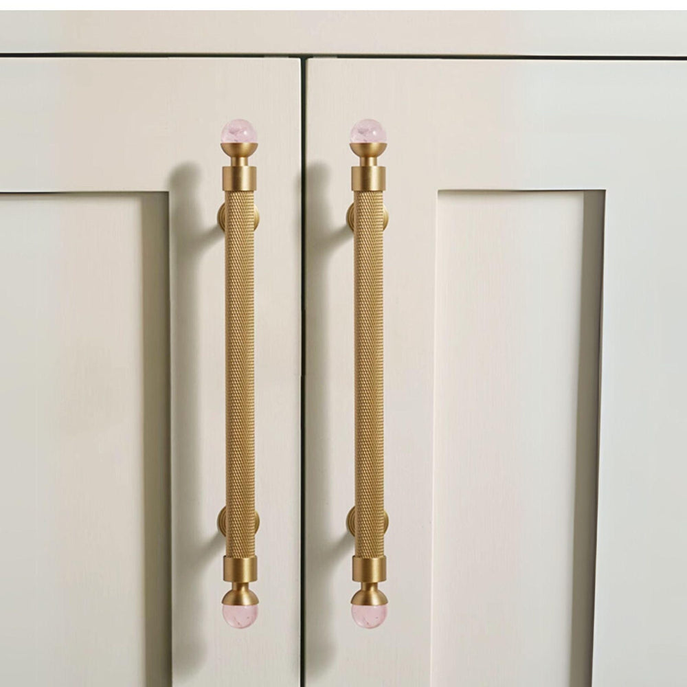 Cabinet doors with gold handles featuring pink glass knobs on a light beige background.